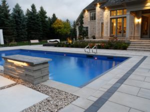 front view of home with stone stairs with greenery behind yard lighting and pool