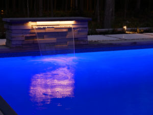 night lit pool with one water fountain pouring into it