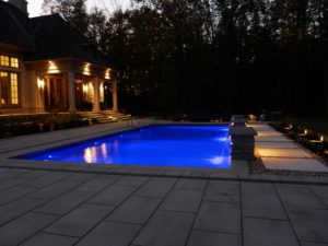 night lit pool with stone patio and back of home